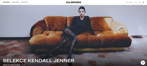 Kendall Jenner sedící na hnědém gauči v černém svetru a ve vzorovaných punčochách