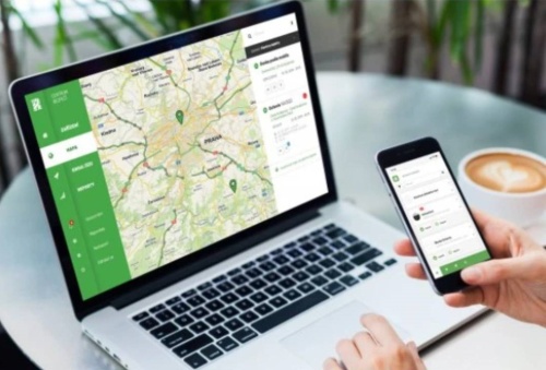 Rex - člověk držící mobil v ruce a na notebooku otevřené mapy a káva na stole