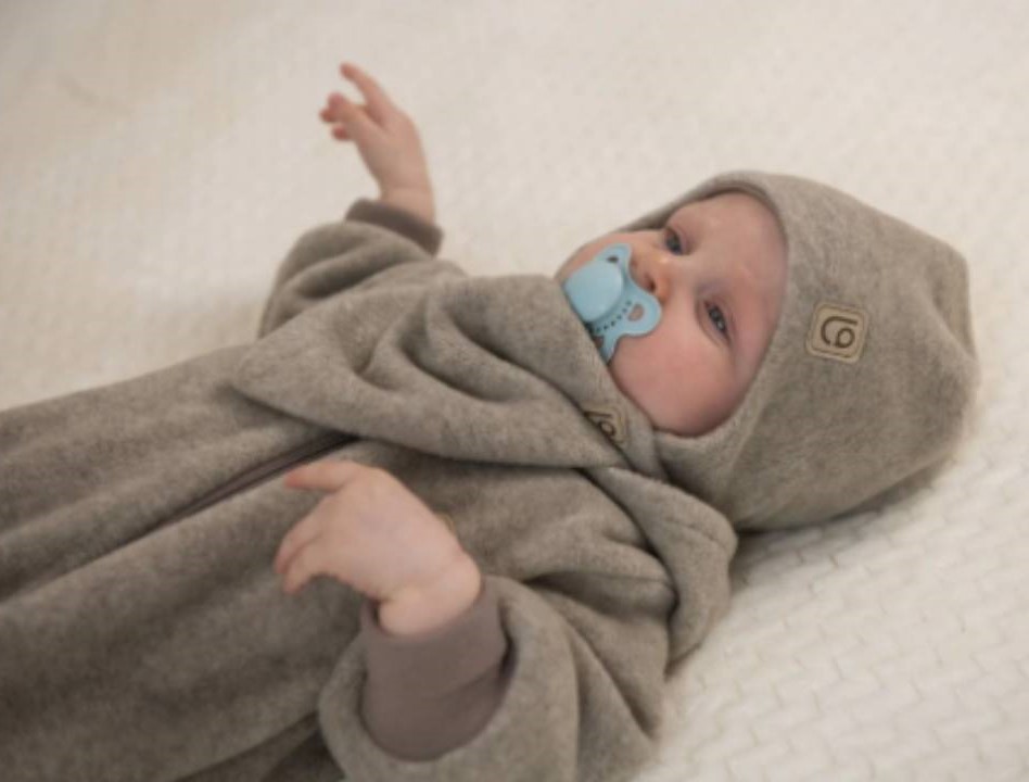 dieťatko v čiapočke a svetríku s dudlíkom ležiace na posteli