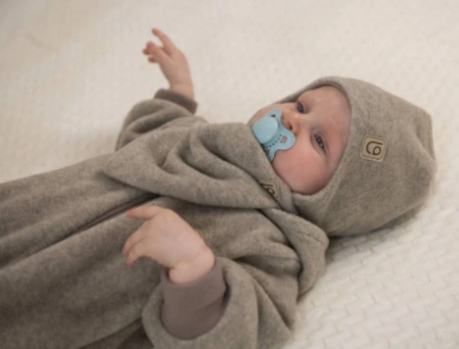 dieťatko v čiapočke a svetríku s dudlíkom ležiace na posteli