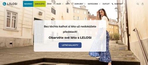 žena v bílém topu a modrobílých širokých kalhotách na ulici mezi domy