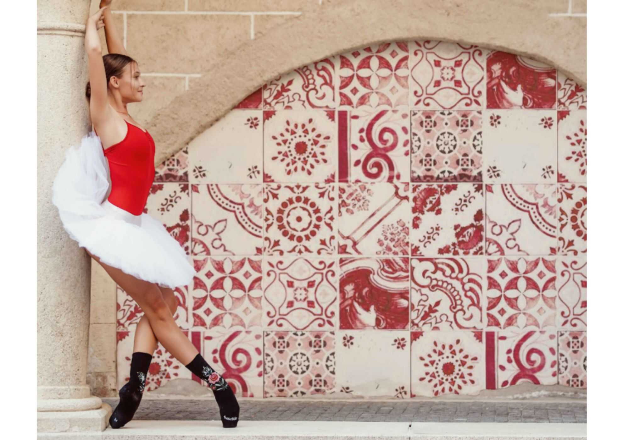 Fusakle - baletka v červeném topu, bílé sukni a v ponožkách před červeno-bílou stěnou