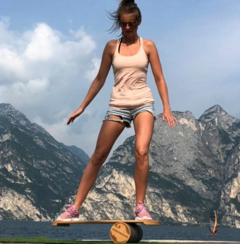 žena na balanční desce s jezerem a horami za zády