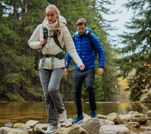 žena v bledé bundě s batohem a v šedých kalhotách a muž v modré bundě a tmavých kalhotách s batohem na túře v lese