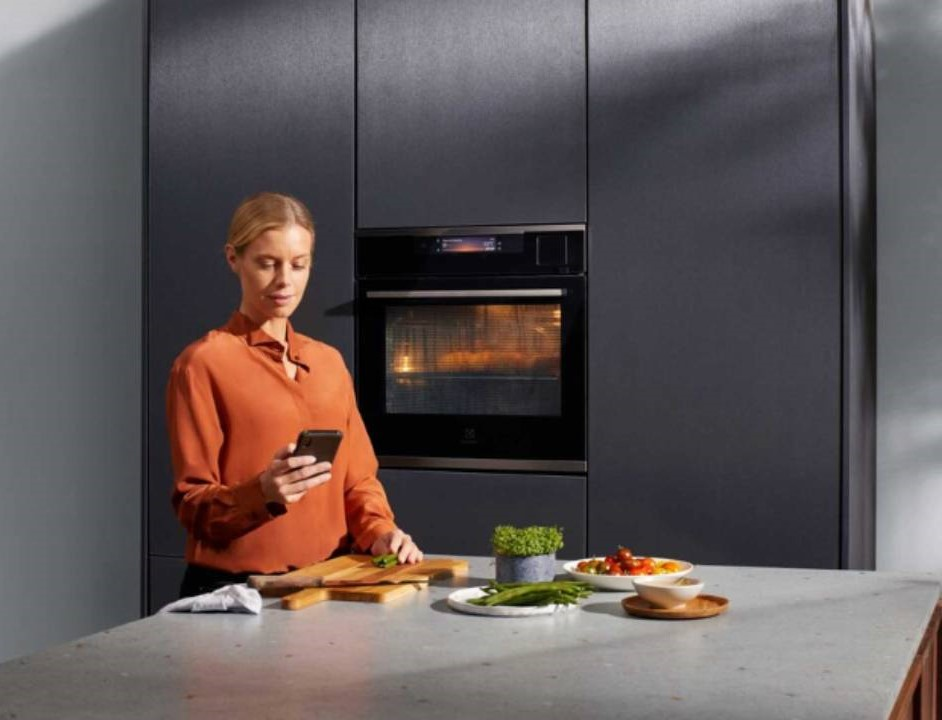 žena v kuchyni u trouby s mobilem v ruce