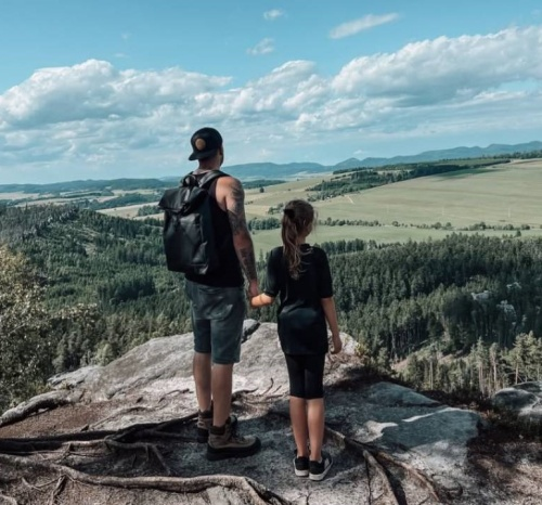 Bushman - muž s batohem a kšiltovkou ve sportovním oblečení drží za ruku dívku ve sportovním outfitu