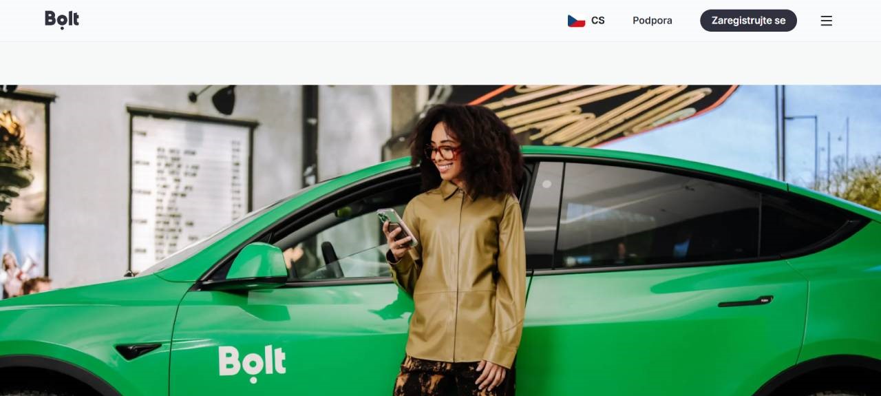 zelené auto s nápisem a před ním žena s mobilem v ruce