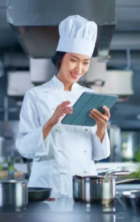 kuchařka v kuchyni s hrncem před sebou dívá do tabletu