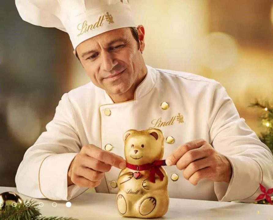 muž v rondonu a s kuchařskou čepicí uvazující mašličku čokoládovému mackovi