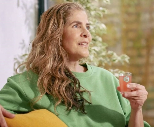 žena sedící na gauči s tekutým oranžovým probiotikem ve skleničce