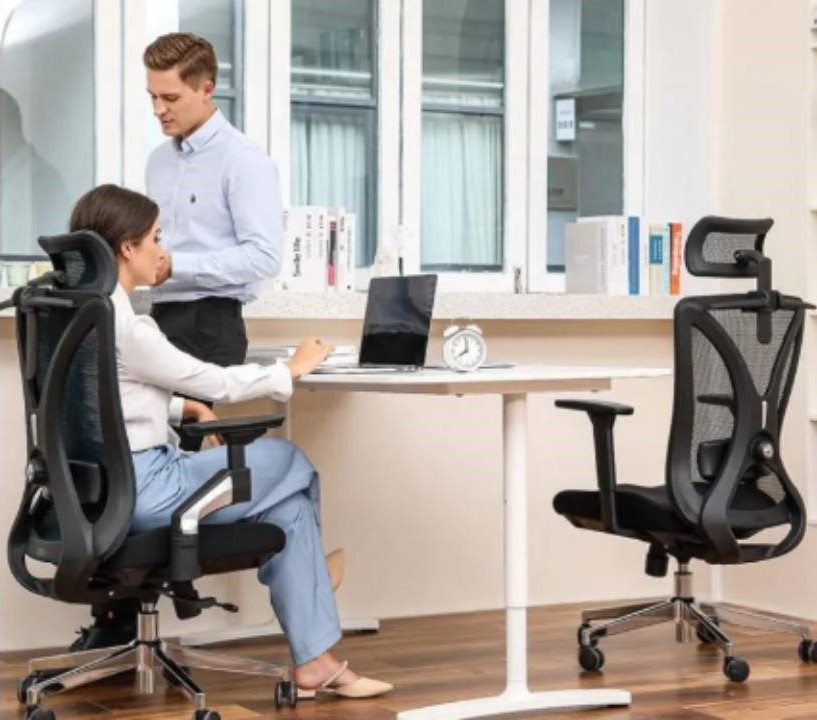 muž stojící u stolu a žena sedící na židli za stolem v kanceláři