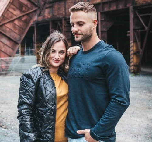 žena ve žlutém tričku a černé bundě objímající muže v tmavě zeleném svetru