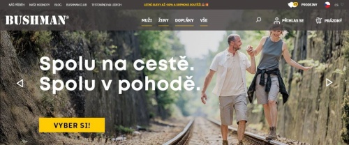 Bushman - muž ve sportovním oblečení drží za ruku ženu v outdoor oblečení, která kráčí po kolejnici