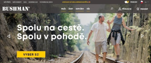 Bushman - muž ve sportovním oblečení drží za ruku ženu v outdoor oblečení, která kráčí po kolejnici