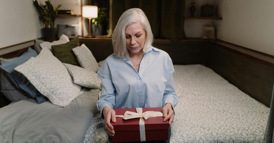 zena-sedici-na-posteli-s-darkem-v-rukou